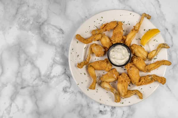 Crispy fried frog legs garnished with parsley, served with a lemon wedge and creamy dipping sauce — a unique and bold seafood appetizer.