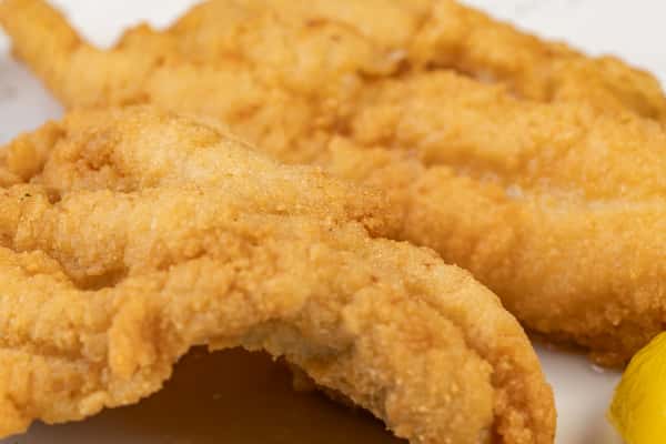 Close-up of golden fried fish fillets with a crispy breaded coating, served with a lemon wedge — a classic seafood favorite.