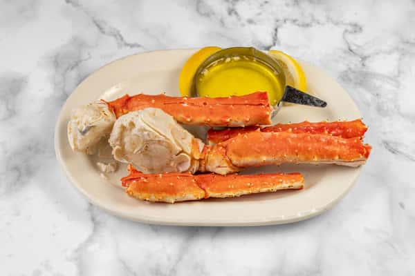 Plate of steamed king crab legs served with lemon wedges and a cup of melted butter — a classic and indulgent seafood dish on a marble backdrop.