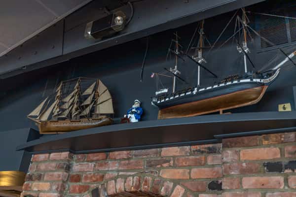 Nautical-themed decor featuring detailed model ships and a sailor figurine displayed on a shelf above a rustic brick fireplace — enhancing the maritime ambiance inside Sindbad's Restaurant in Detroit.