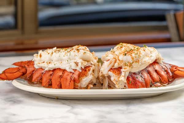 Plated twin lobster tails topped with seasoned butter and parsley, served open-faced for a decadent seafood presentation — a signature fine dining option at Sindbad's.