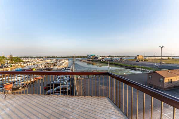 Scenic view of the waterfront marina from Sindbad's Restaurant balcony, overlooking docked boats, a peaceful waterway, and a spacious parking area under a clear sky.