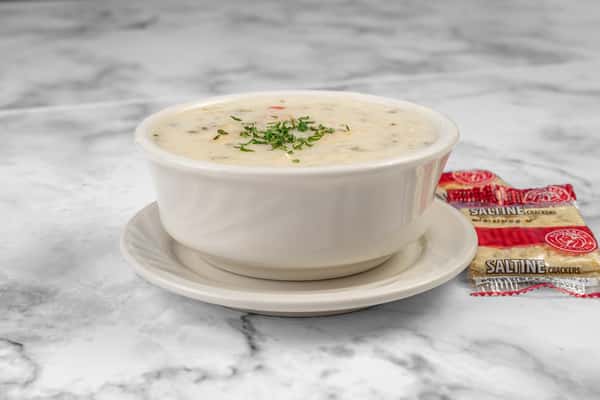 Creamy New England clam chowder garnished with parsley, served in a white bowl with packets of saltine crackers — a comforting seafood soup.