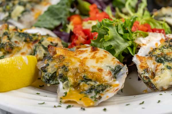 Cheesy baked Oysters Rockefeller topped with spinach and herbs, served alongside fresh greens and a lemon wedge — a rich and savory seafood appetizer.