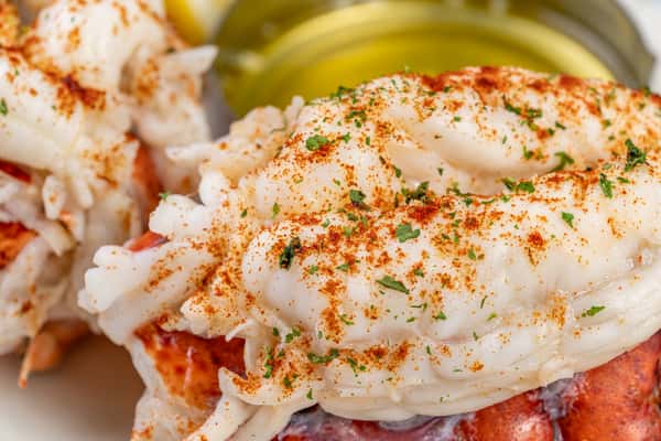 Macro view of a broiled lobster tail topped with drawn butter, paprika, and parsley, highlighting the juicy, tender texture of the shellfish.