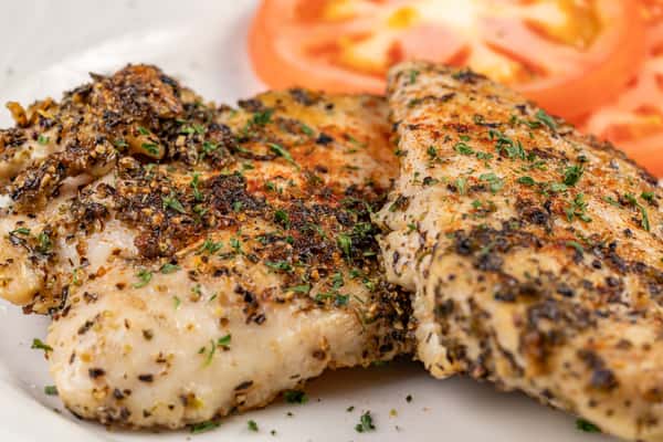 Close-up of herb-seasoned grilled chicken breasts garnished with chopped parsley, served with fresh tomato slices — a healthy and flavorful protein option ideal for low-carb or Mediterranean-style dining.