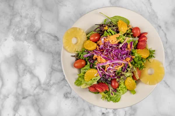 Colorful tropical salad with mixed greens, shredded carrots, red cabbage, cherry tomatoes, strawberries, mandarin oranges, and pineapple rings — a vibrant, refreshing vegetarian option.