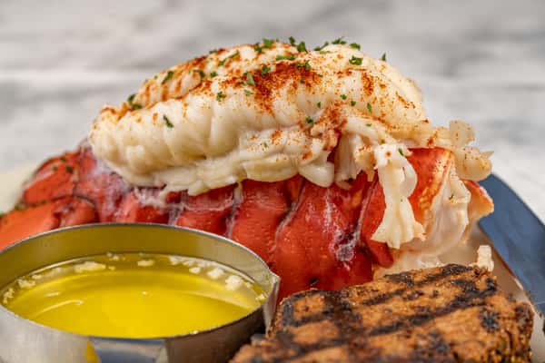 Surf and turf entrée featuring a broiled lobster tail topped with paprika and parsley, served alongside grilled steak and a ramekin of melted butter — a classic seafood and steakhouse pairing.