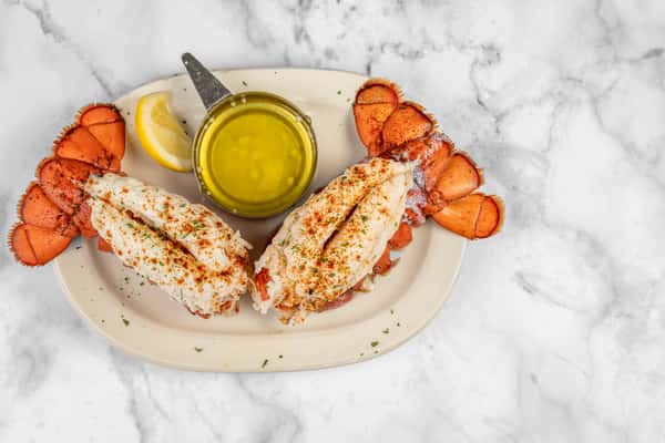 Overhead shot of two broiled lobster tails garnished with paprika and parsley, served with a lemon wedge and warm clarified butter — a luxurious seafood dish.