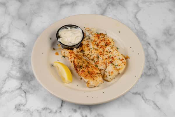Plated grilled white fish fillets seasoned with herbs, served with tartar sauce and a lemon wedge — a light and flavorful seafood entrée on a white plate.