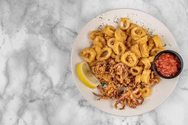 Plated fried calamari rings and tentacles with a golden-brown crunch, served with marinara dipping sauce and a lemon wedge — a popular seafood appetizer.