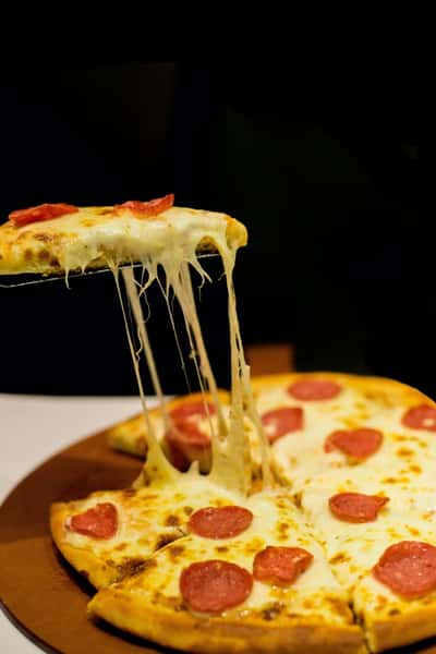 Pepperoni pizza with melted cheese stretching as a slice is lifted, set against a dark background for dramatic contrast.