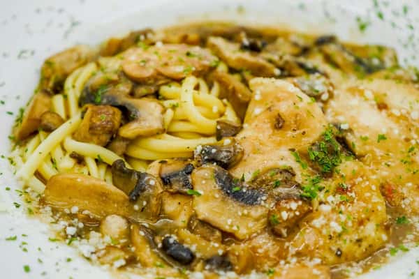 Chicken marsala with mushrooms and linguine pasta, topped with parsley and Parmesan in a savory brown wine sauce.