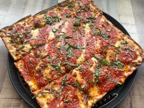 Crispy rectangular pizza topped with tomato sauce, fresh basil, and melted cheese, sliced into even squares.