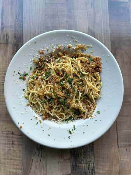 Spaghetti tossed with toasted breadcrumbs, parmesan cheese, and fresh herbs on a white plate over a rustic wooden table.