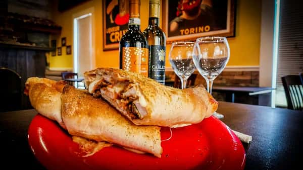 Stuffed calzones filled with meats and cheese on a red plate, served beside wine bottles and glasses in a rustic dining setting.