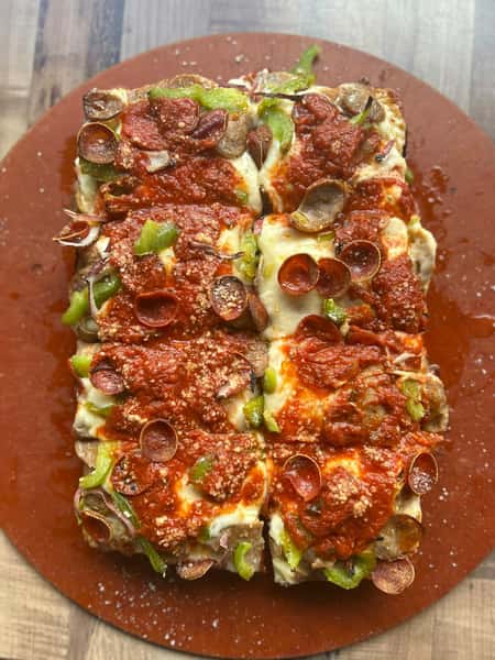 Rectangular Detroit-style pizza topped with melted cheese, marinara sauce, pepperoni, sausage, green peppers, and red onions.