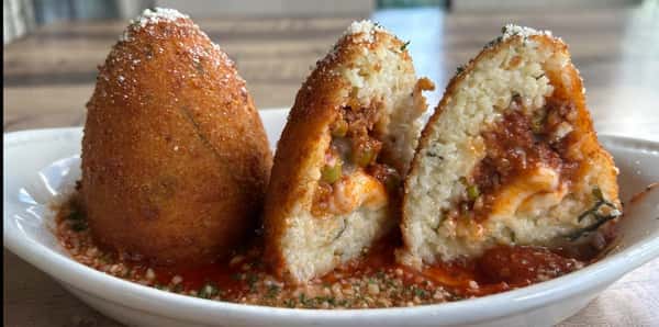 Crispy golden arancini stuffed with meat, peas, and cheese, served over marinara sauce in a white dish.