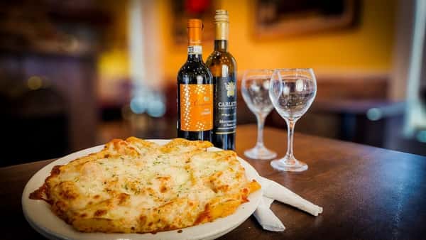 Cheesy garlic bread served on a white plate beside two bottles of wine and empty wine glasses in a cozy restaurant setting.
