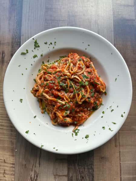 Plate of spaghetti topped with marinara sauce and sprinkled with chopped parsley on a rustic wooden table.