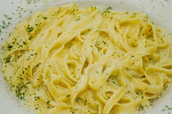 Creamy fettuccine Alfredo topped with grated Parmesan and chopped parsley on a white plate.