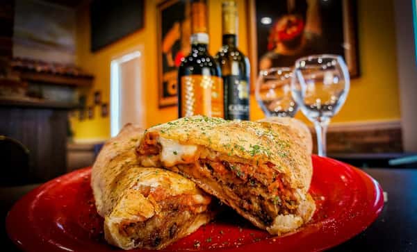 Golden-brown calzone stuffed with melted cheese, ground meat, and marinara sauce, garnished with herbs on a red plate.