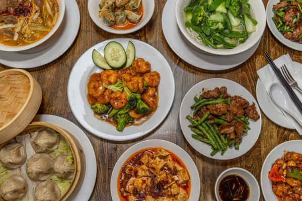 Assorted Chinese stir-fry dishes served on white plates, including spicy chicken with chili sauce, shrimp and broccoli in garlic brown sauce, Kung Pao chicken with bell peppers and peanuts, beef with scallions, and beef with green beans, all presented on a rustic wooden table.