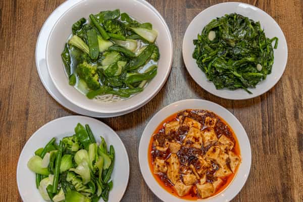 Assorted Chinese stir-fry dishes served on white plates, including spicy chicken with chili sauce, shrimp and broccoli in garlic brown sauce, Kung Pao chicken with bell peppers and peanuts, beef with scallions, and beef with green beans, all presented on a rustic wooden table.