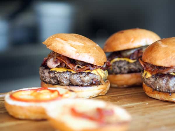 Three cooked hamburgers with bacon and condiments