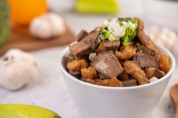 Roasted beef and pork in a bowl topped with chives