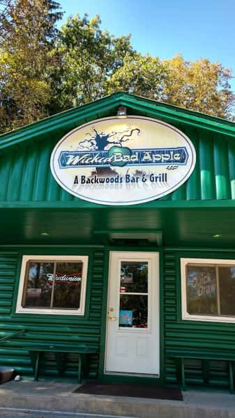 Wicked Bad Apple Backwoods Bar & Grill green exterior with bold logo signage above the entrance, surrounded by trees—inviting Northwoods restaurant and local tavern destination.