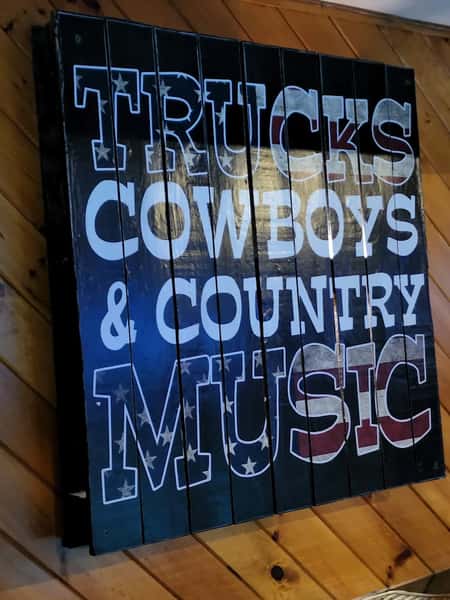 Trucks, Cowboys & Country Music" rustic wooden wall sign with American flag design—country-themed bar decor enhancing the laid-back tavern vibe
