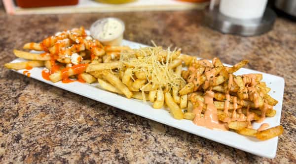 Three varieties of fries on a white platter: buffalo chicken fries, parmesan truffle fries, and cajun fries.