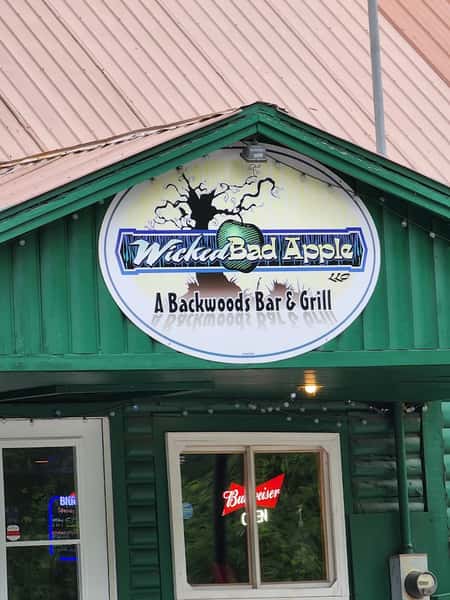 Wicked Bad Apple Backwoods Bar & Grill exterior sign mounted on a rustic green building, featuring a bold apple logo and Northwoods-style branding above the entrance—classic local tavern and grill atmosphere.