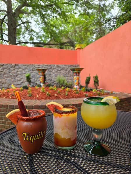 three cocktails showing in outdoor seating area with stone fountain
