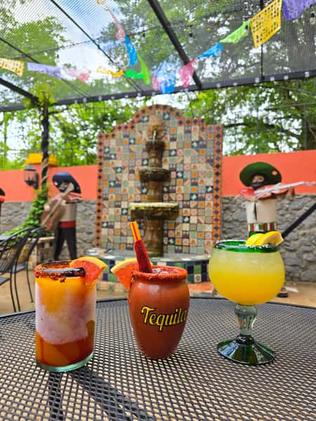 three cocktails showing in outdoor seating area with stone fountain