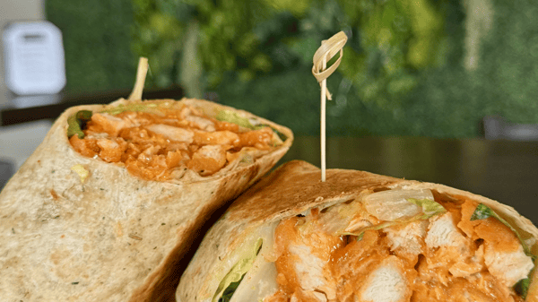 Grilled chicken wrap cut in half, filled with seasoned chicken, lettuce, and sauce, served on a wooden pick.