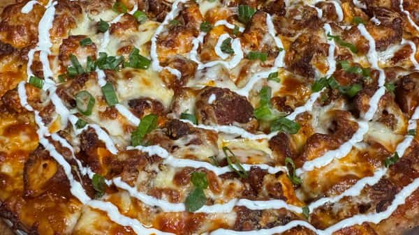 Pizza topped with sausage, melted cheese, and drizzled sauce, finished with green onions.