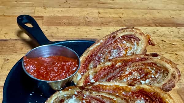 Sliced pizza bread served with a side of marinara sauce on a wooden board