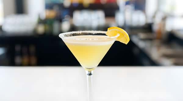 Martini glass with a pale yellow drink, a sugar-rimmed edge, and a lemon slice garnish.
