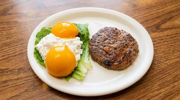 Hamburger patty with cottage cheese, peaches, and lettuce on a white plate.