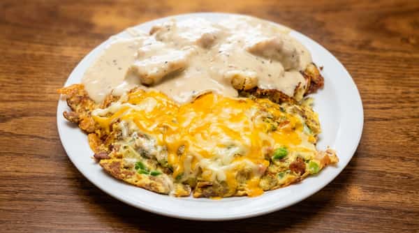 Omelet with melted cheddar cheese and diced vegetables, beside biscuits covered in sausage gravy.