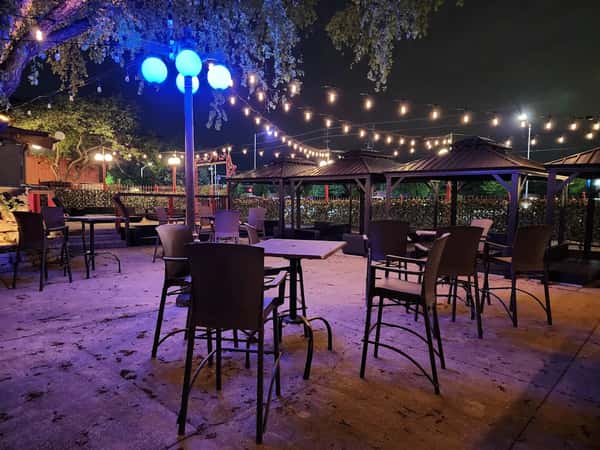 Outdoor patio with string lights, gazebo seating, and blue globe lamps under trees on a calm night.