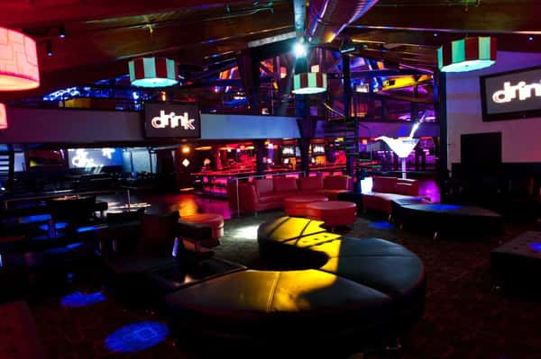 Colorful nightclub lounge with vibrant lighting, modern seating, and illuminated decor, including "drink" signs on the walls.