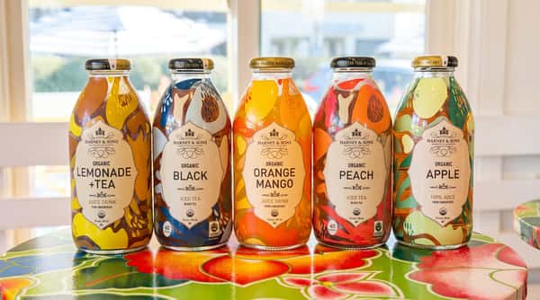 Five Harney & Sons organic juice and iced tea bottles on a colorful floral table.