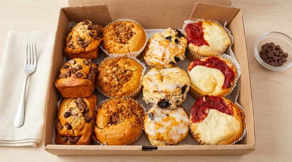 An assortment of 12 muffins, including chocolate chip, crumb, blueberry with glaze, and pizza muffins, in a box.