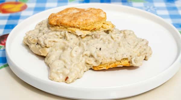 Biscuits and gravy on a white plate, with a blue and white checkered tablecloth visible.
