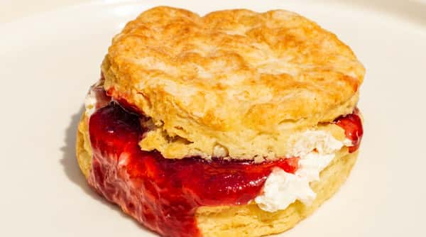 Split biscuit with strawberry jam and whipped cream filling on a white plate.