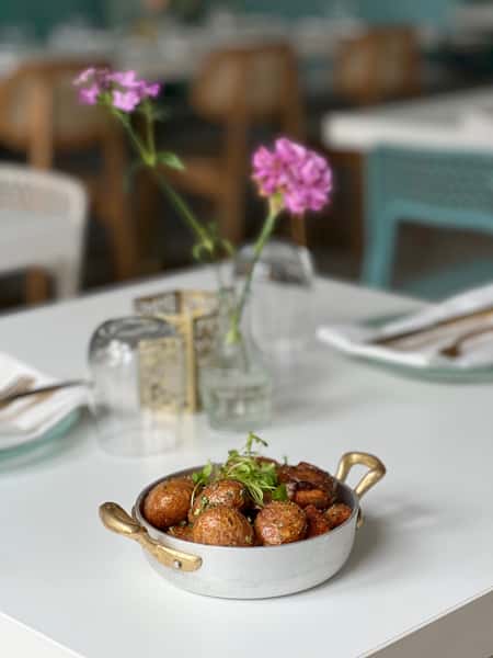 Golden roasted Lebanese potatoes garnished with fresh herbs, served in a traditional pan on a modern dining table at Lira House in Wynwood, Miami.