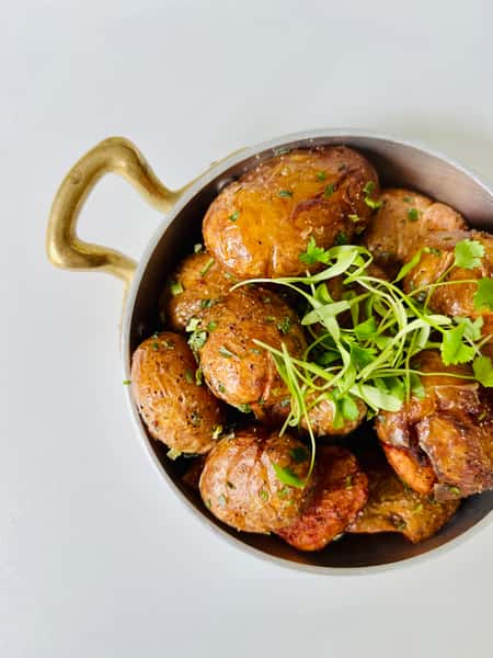 Crispy roasted baby potatoes tossed with herbs and microgreens, served in a brass-handled pan at Lira House, an authentic Lebanese restaurant in Wynwood, Miami.